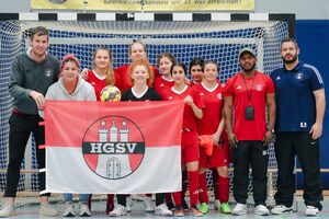Ein paar Fußballspielerinnen und Trainer stehen mit einer HGSV-Flagge vor dem Tor.