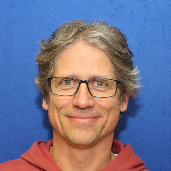 David Galling Eine Person mit kurzen grauen Haaren und Brille ist vor einem blauen Hintergrund zu sehen.